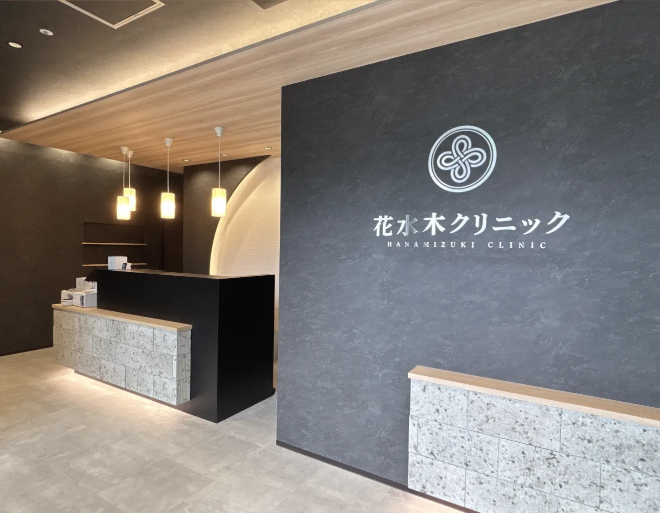 ペンダントライトが並ぶ受付カウンターと花水木クリニックのロゴサイン